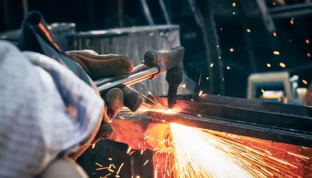 Worker using an oxy-acetylene torch to cut steel in boilermakers workshop.