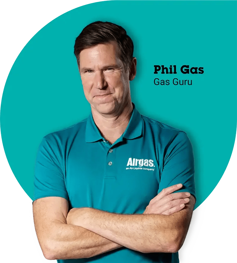 Man in teal Airgas polo with arms crossed, smiling confidently. Text reads 'Phil Gas, Gas Guru' on teal circle backdrop. Tone is professional and approachable.